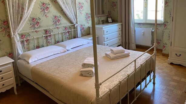 A four-poster bed with a canopy, a bedside table, a dresser, and a window with curtains.