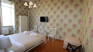 A bedroom with a four-poster bed, a television mounted on the wall, and a floral wallpaper pattern.