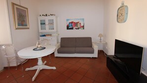 A living room with a white table, a grey sofa, a TV, and a clock on the wall. - Art Atelier San Pietro app int loc turistica (Roma)
