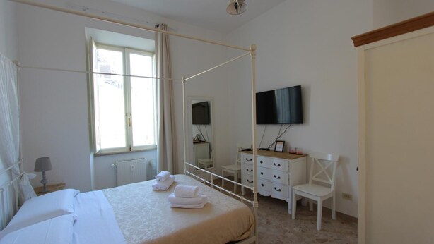A four-poster bed with neatly folded towels, a television mounted on the wall, a white dresser, and a window with curtains. - Art Atelier San Pietro app int loc turistica (Roma)