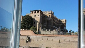 A view of a historic building with a large tower and multiple arches, viewed from a window with a metal railing. - Art Atelier San Pietro app int loc turistica (Roma)