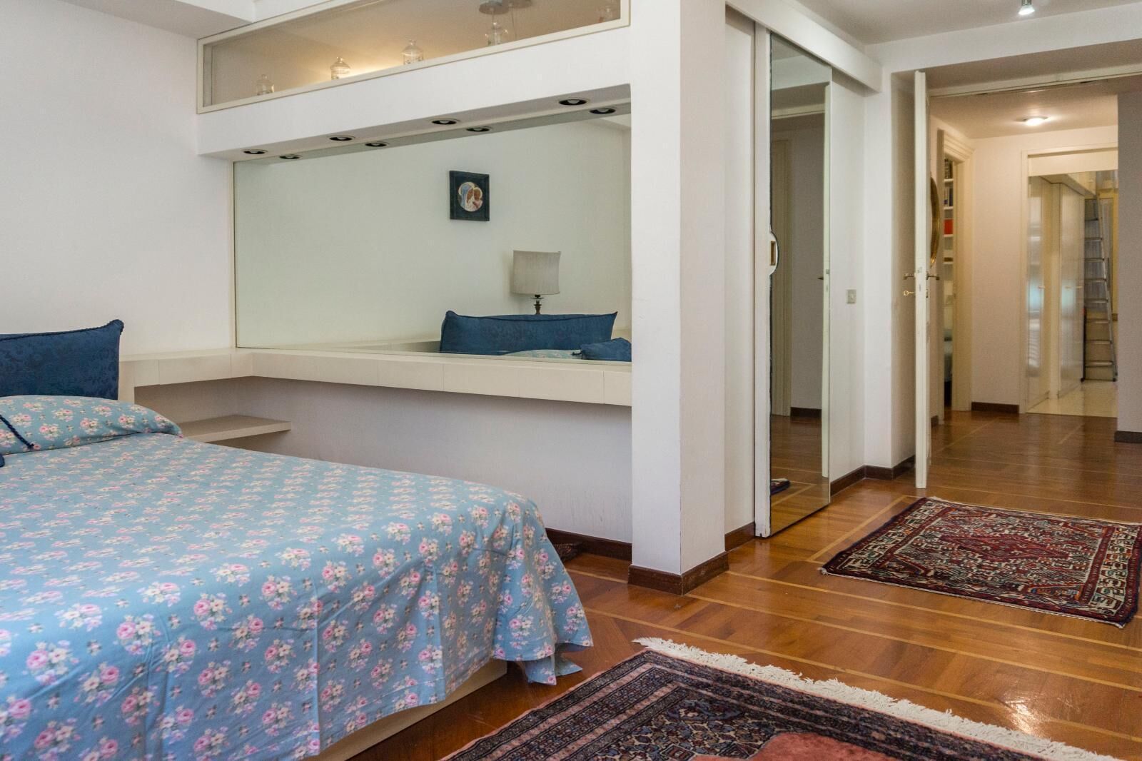 Un dormitorio con cama, mesita de noche, espejo y vestidor.
