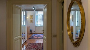 Un pasillo con un espejo grande y ornamentado, suelo de madera y vistas a una habitación con cama y ventana.