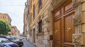 Una calle estrecha con coches aparcados y un edificio de grandes puertas de madera y detalles de piedra.