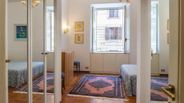 Una habitación con dos camas, una ventana con contraventanas, un escritorio y una silla.