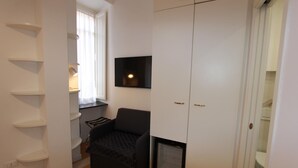 A compact room with a black armchair, a white wardrobe, and a small window with curtains.