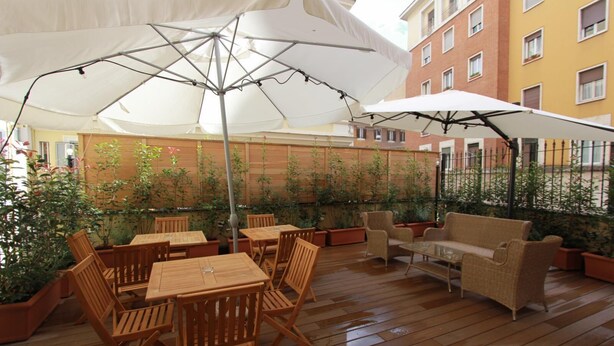 An outdoor patio with wooden tables and chairs, white umbrellas, and potted plants. - Art Atelier Risorgimento guest house c2 (ROMA)