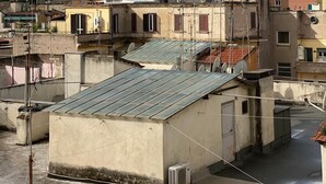Una azotea con paneles solares, un edificio pequeño con antena parabólica y un edificio histórico con cúpula al fondo.