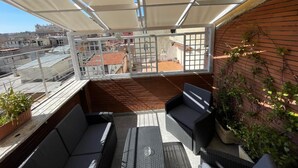 Terraza en la azotea con mobiliario exterior, vistas a la ciudad y una pared de ladrillo con plantas trepadoras.