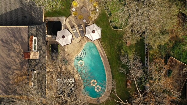 An aerial view of a backyard with a swimming pool, surrounded by trees and a patio area with umbrellas and seating. - Giddy Up Getaway: Pool, Hot Tub & Family Fun! (San Antonio)