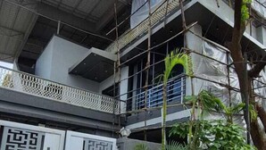A multi-story building with a gated entrance, a concrete pathway, and green waste bins. - HM Villas (Paud)