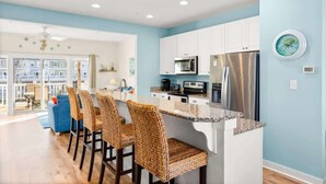A modern kitchen with white cabinets, stainless steel appliances, and a breakfast bar with wicker chairs. - Harborview Retreat Mansion (Ocean City)