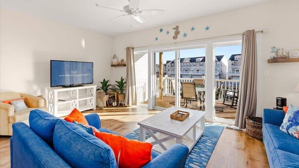 A living room with a television, blue sofas, a coffee table, and a balcony with a view of buildings. - Harborview Retreat Mansion (Ocean City)