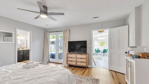 Une chambre moderne équipée d’un lit, d’une télévision, d’un ventilateur de plafond et d’une porte-fenêtre coulissante donnant sur un espace extérieur.
