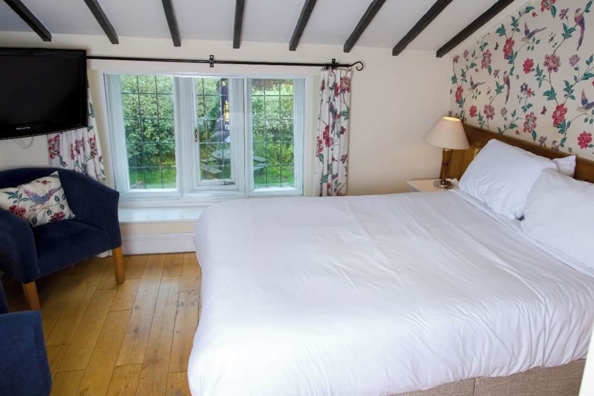 Een slaapkamer met een groot bed, een stoel, een aan de muur bevestigde televisie en een raam met gordijnen.