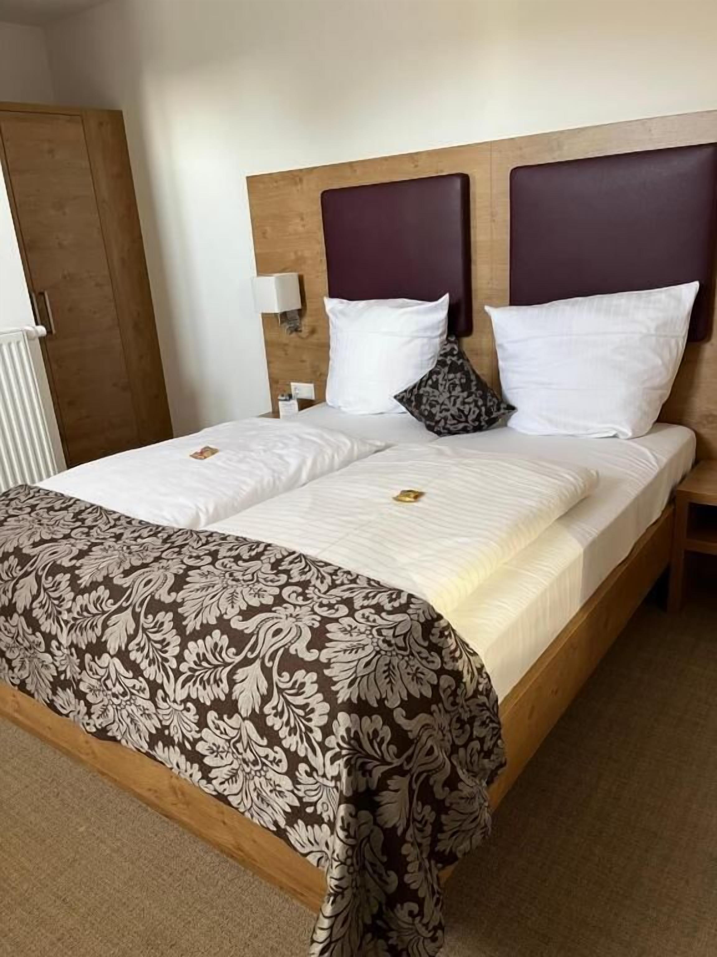 A double bed with a floral-patterned bedspread, two white pillows, a dark headboard, and a bedside table with a lamp.
