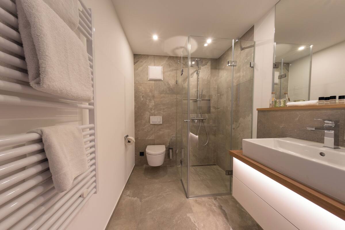 A modern bathroom with a glass-enclosed shower, a white toilet, and a large sink with a wooden countertop.