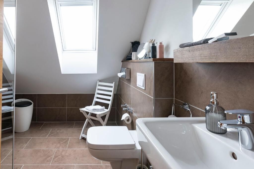 A modern bathroom with a white toilet, a sink, and a shower area. There is a towel rack and a small window providing natural light.