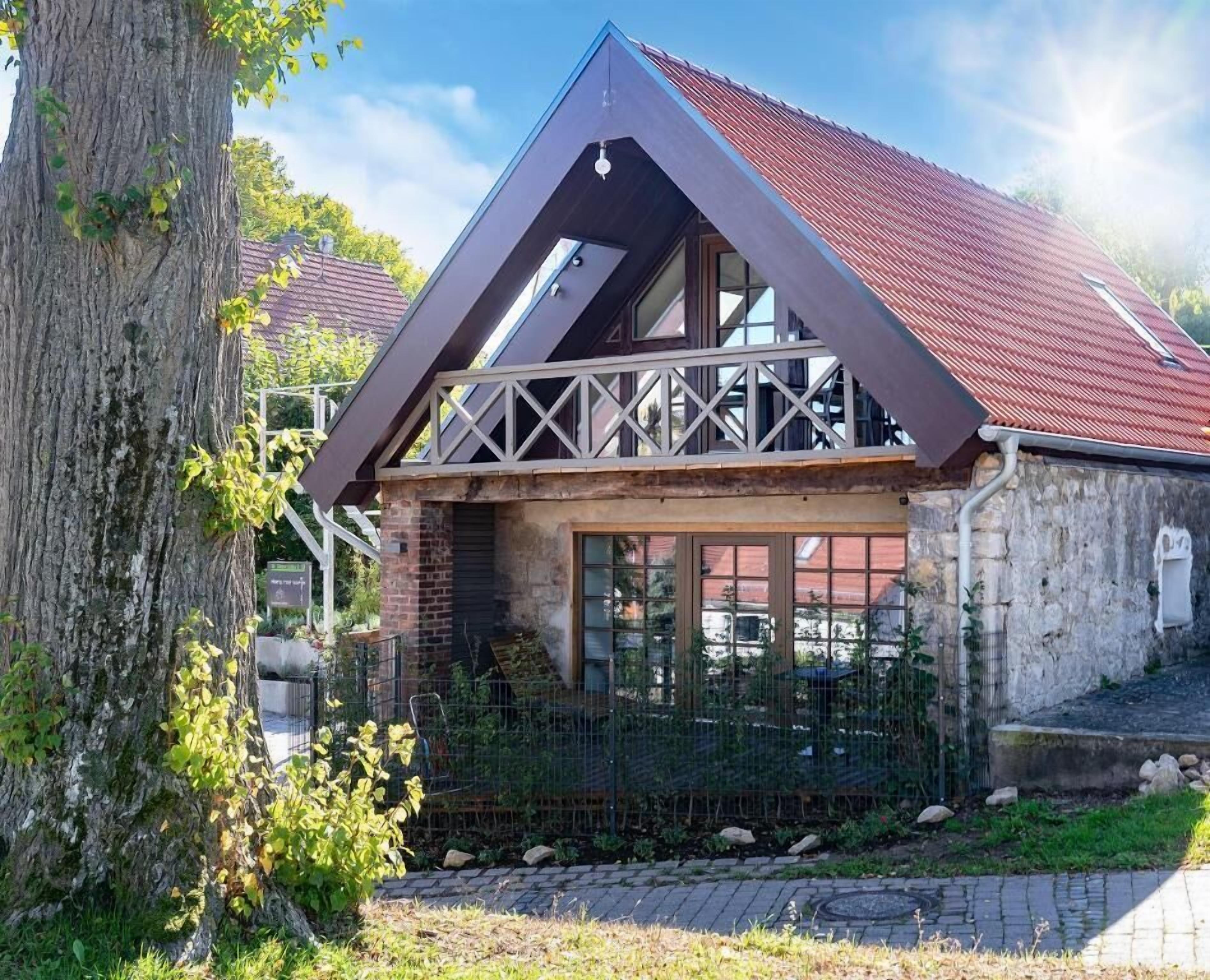 A house with a sloped roof, a balcony with a railing, and a brick facade.