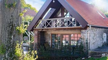 A house with a sloped roof, a balcony with a railing, and a brick facade.