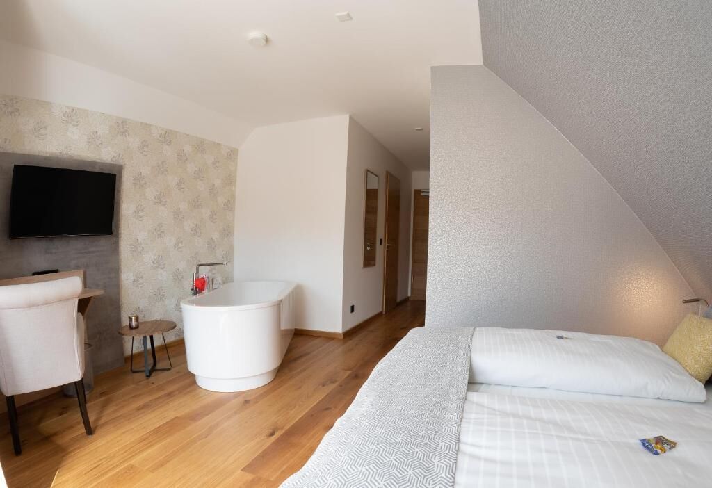 A modern bedroom with a large bed, a built-in bathtub, a flat-screen TV, and a small table.