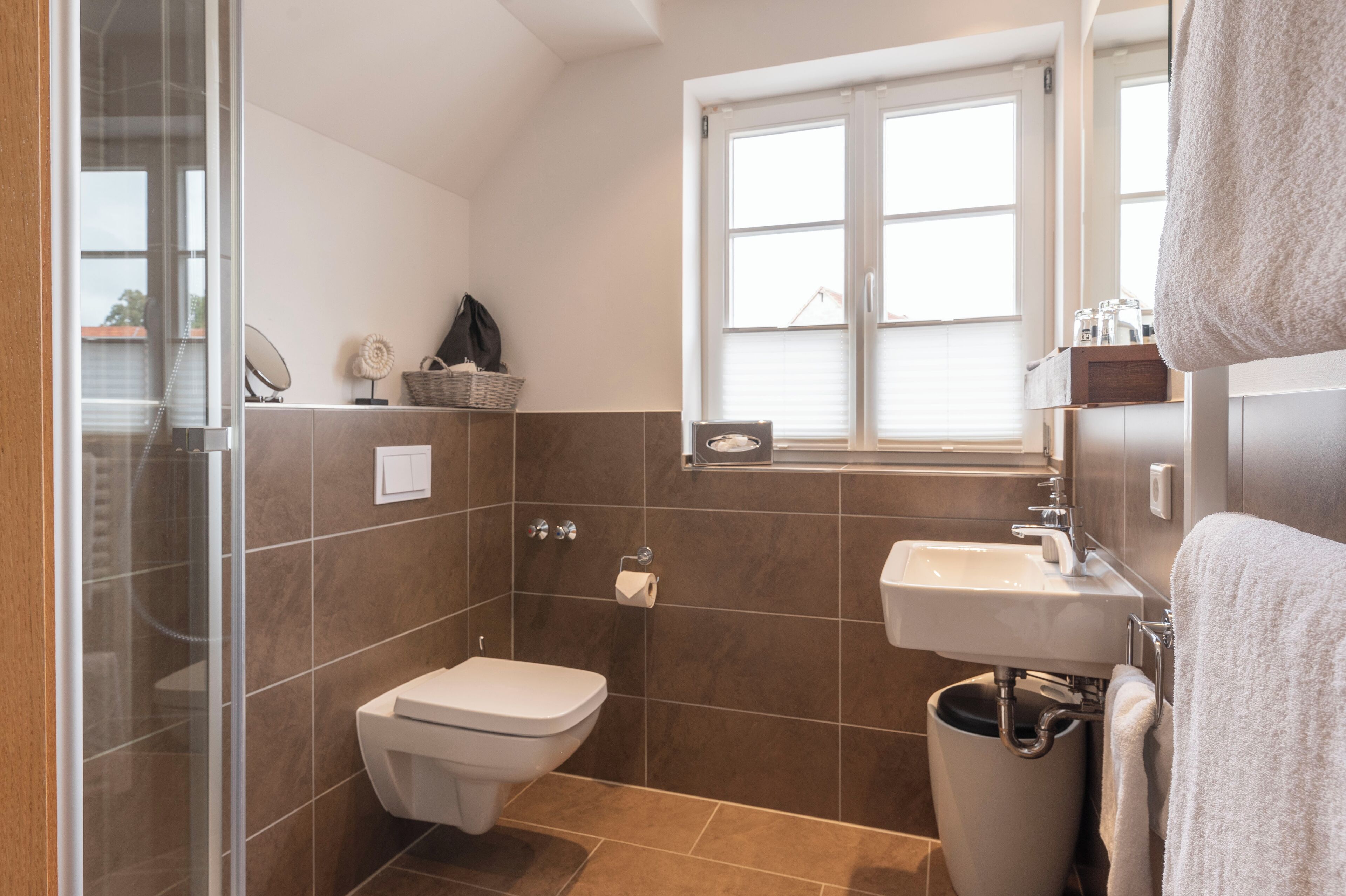 A modern bathroom with a glass shower enclosure, a toilet, a sink, and a window providing natural light.