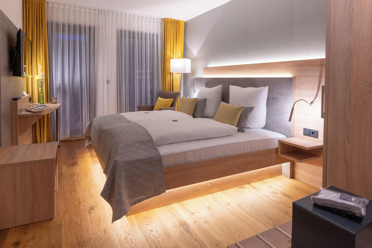 A modern hotel room with a large bed, wooden floor, and a desk with a lamp.
