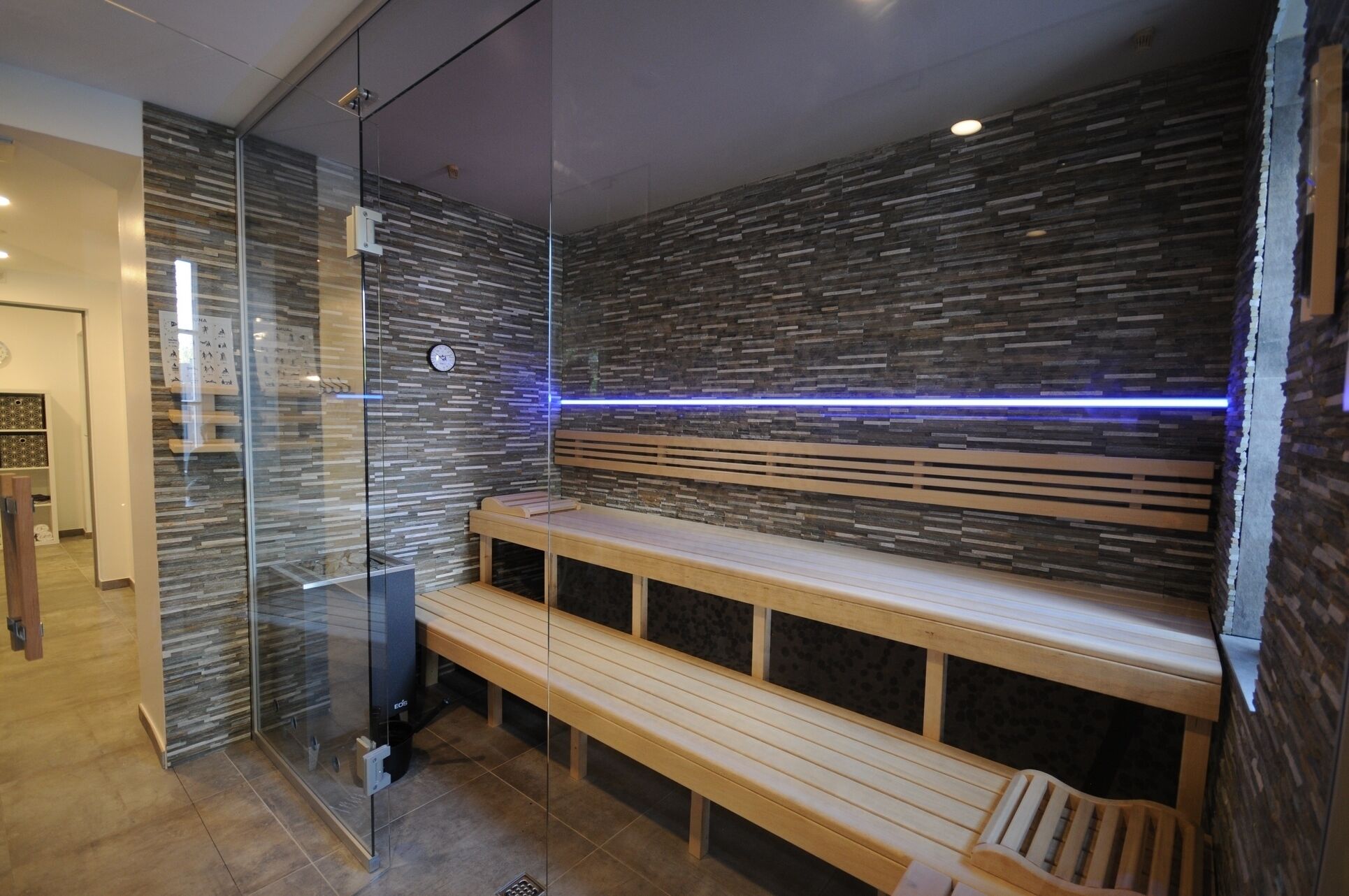 A modern sauna with a wooden bench, glass walls, and a blue-lit ceiling.
