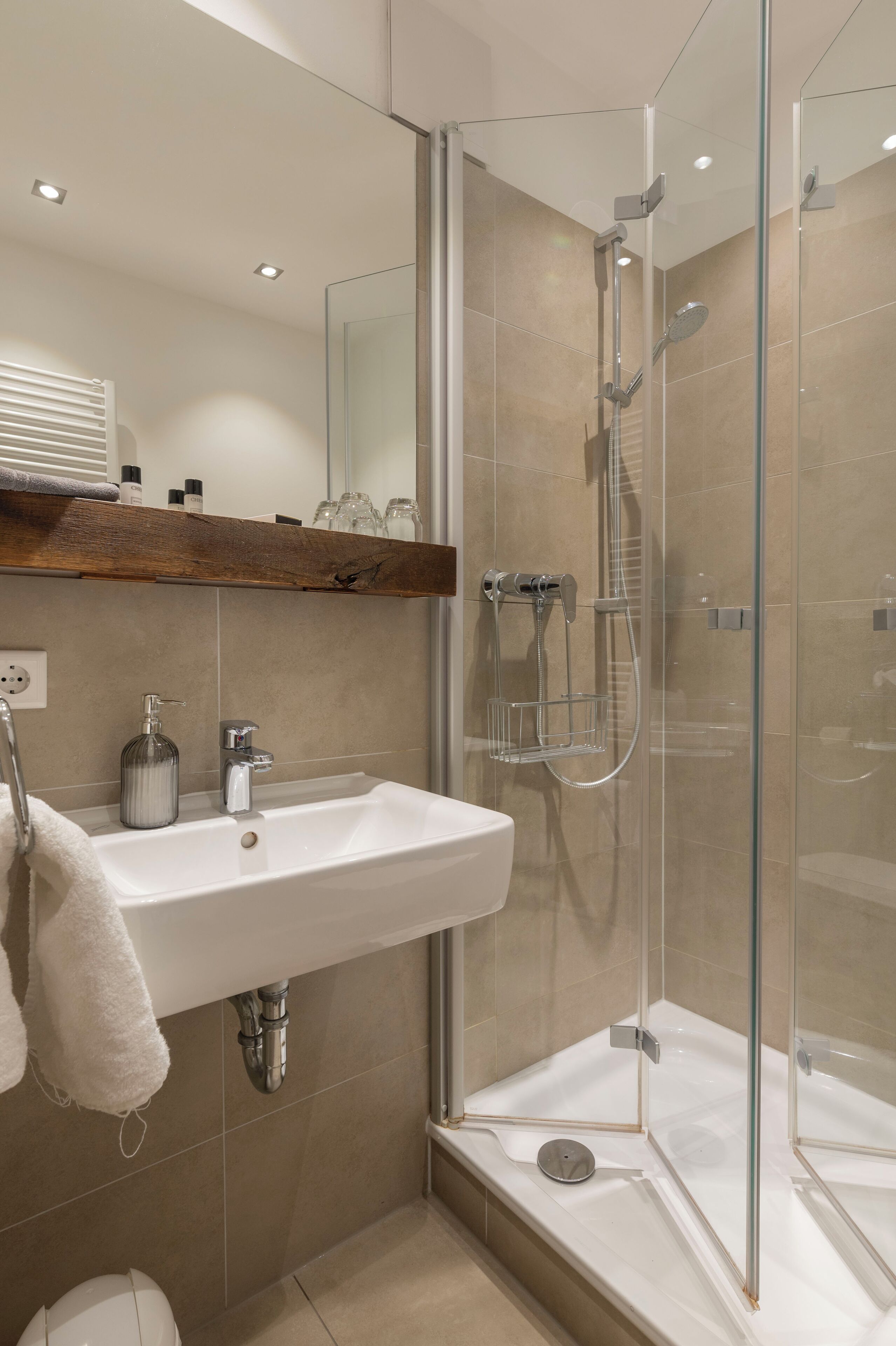 A modern bathroom with a glass-enclosed shower, a white sink, and a wooden shelf above the sink.