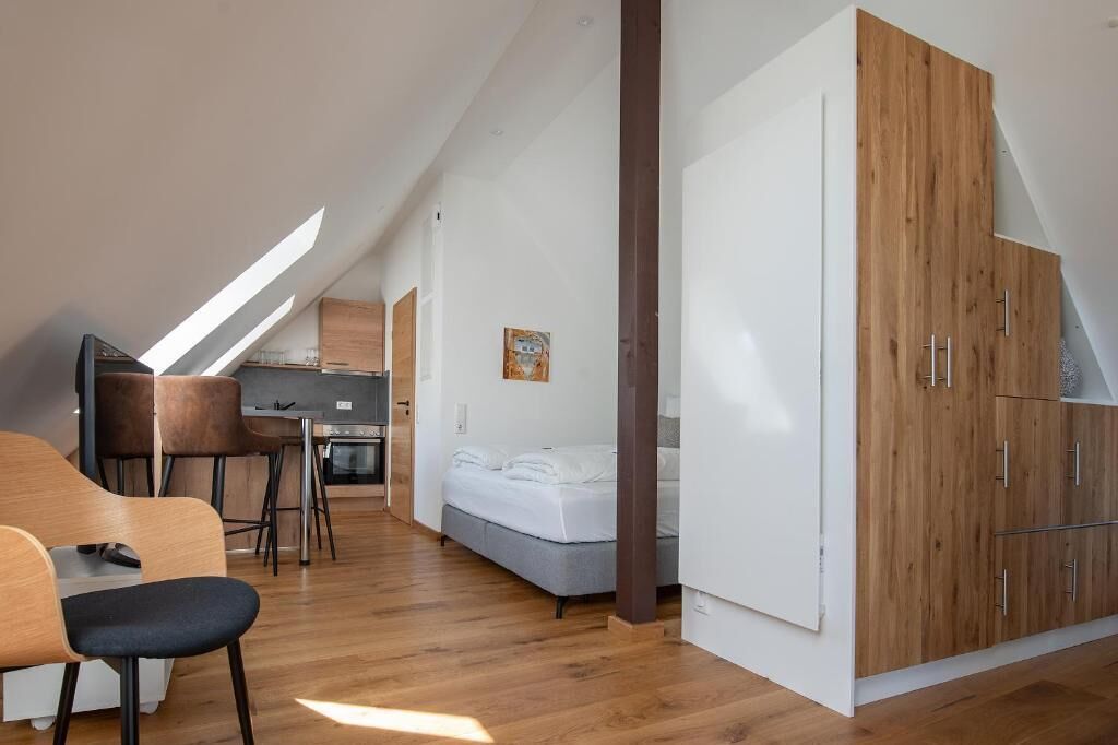 Un dormitorio tipo loft moderno con techo inclinado, armario de madera, cama y zona de comedor con sillas y mesa.