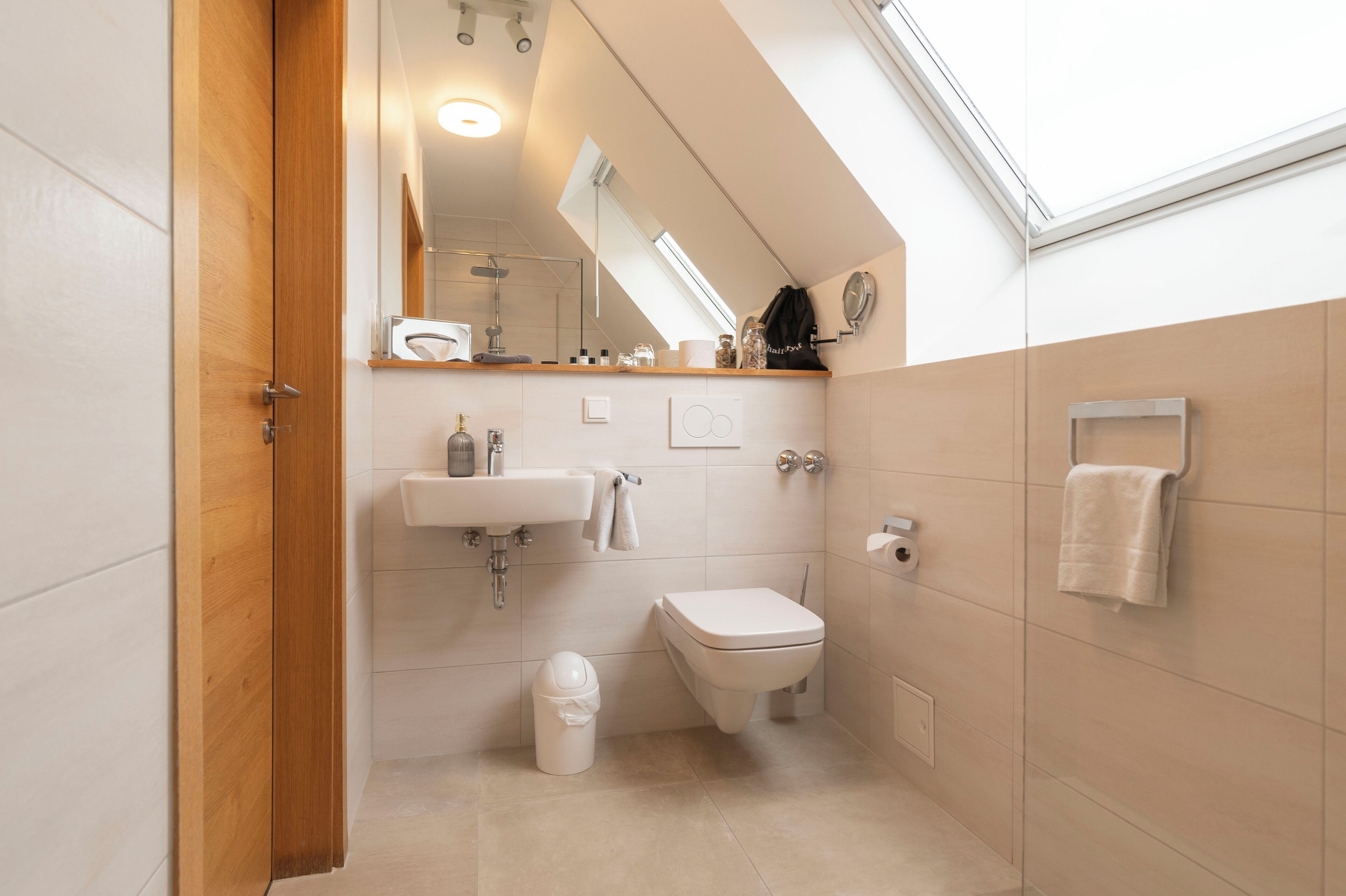 Un baño moderno con tragaluz, lavamanos, inodoro y un perchero para toallas.