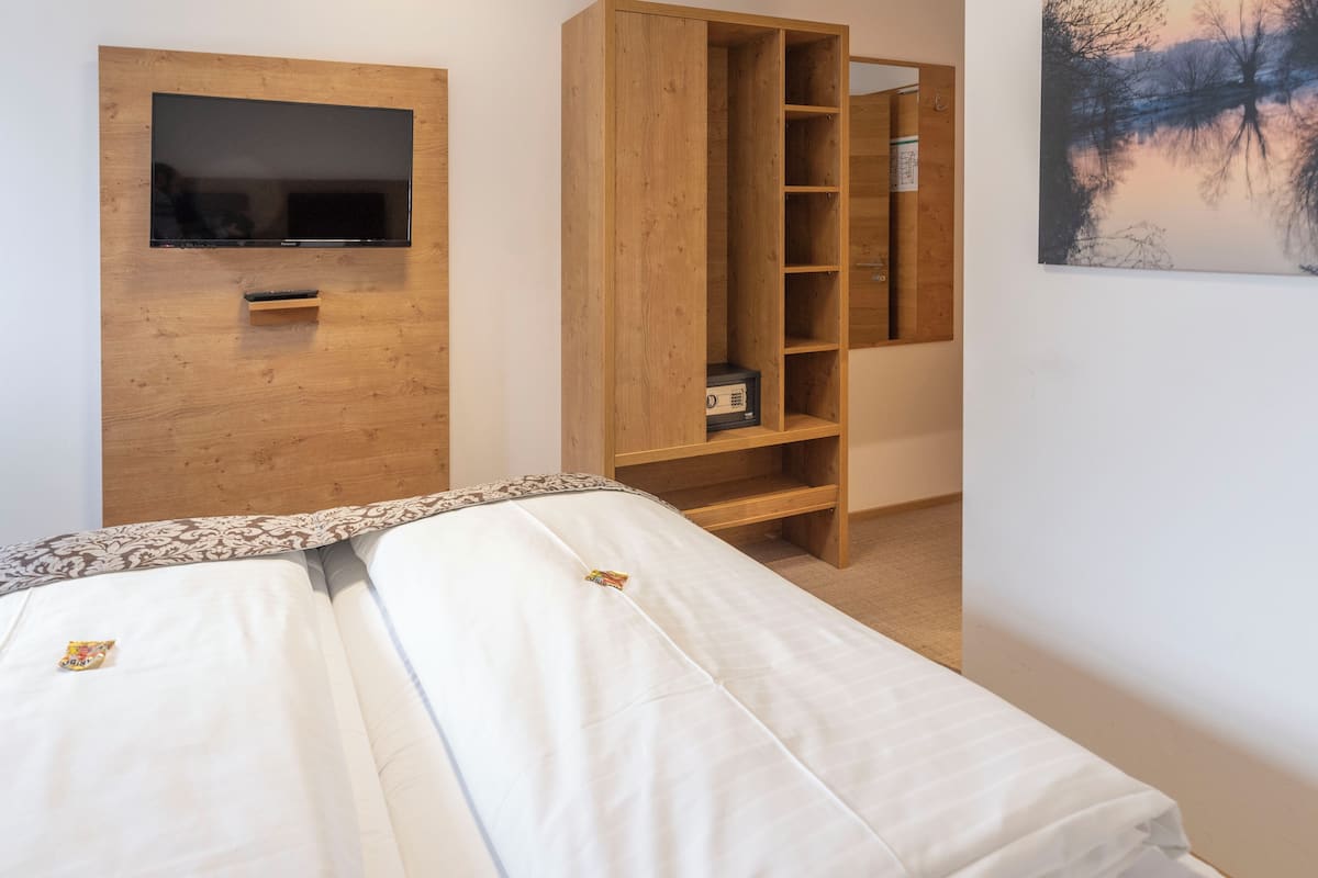 A bedroom with a bed, a TV mounted on a wooden wall, a wooden wardrobe, and a painting on the wall.