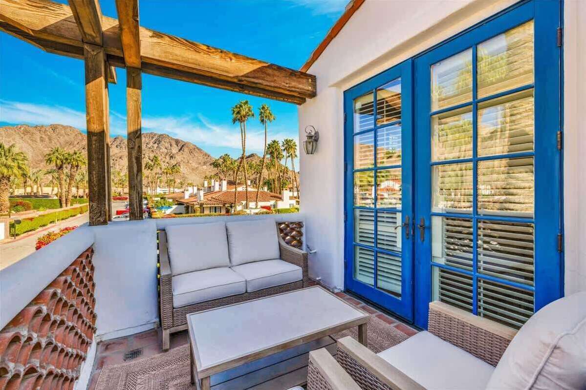A balcony with a white sofa, a small table, and a blue door with shutters.