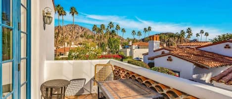 A terrace with a table and chairs, overlooking a residential area with palm trees and a mountain.