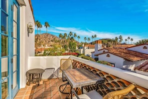 Una terraza con mesa y sillas, con vista a una zona residencial con palmeras y una montaña.