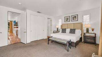 Una habitació d'hotel amb un llit gran, una banca, una taula de nit i una làmpada penjada a la paret.