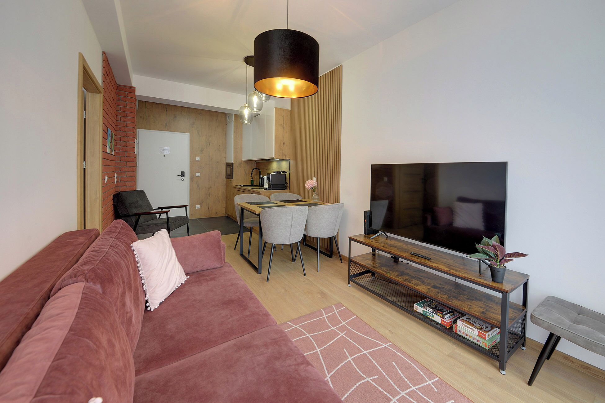 A modern living room with a red sofa, a dining area with a table and chairs, a TV on a wooden stand, and a kitchen in the background.