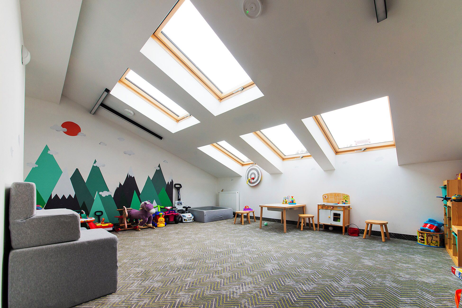 A spacious room with high ceilings, skylights, a play area with toys, and a target on the wall.