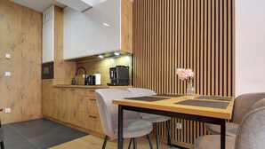 Eine moderne Küche mit Holzausstattung, einer eingebauten Mikrowelle und einer Kaffeemaschine. Ein Essbereich mit einem Holztisch und zwei Stühlen ist ebenfalls vorhanden.