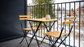 Ein Balkon mit Holztisch und Stühlen, einer Vase und Blick auf eine verschneite Landschaft mit Häusern.