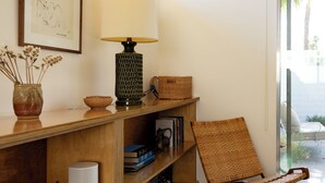 Une pièce avec une bibliothèque en bois, un fauteuil en osier, une lampe et un tableau encadré accroché au mur.