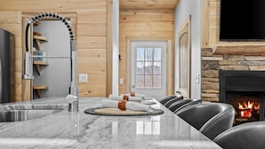 A modern kitchen with a large island, a fireplace, and a stone wall. - Bear Paw Getaway - Beech luxury with hot tub, fire pit (Beech Mountain)