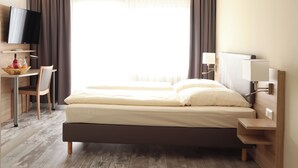 A hotel room with a bed, a desk with a chair, a television, and a window with curtains.