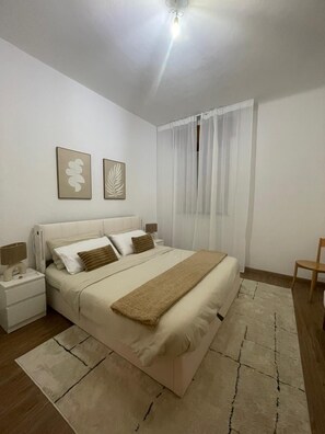 A neatly arranged bedroom with a bed, bedside tables, a lamp, and two wall-mounted artworks.