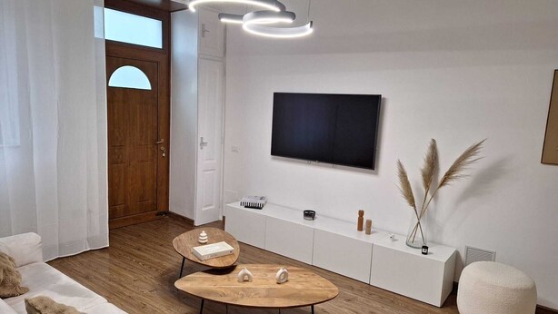 A modern living room with a wooden floor, white furniture, a flat-screen TV, and a decorative vase with pampas grass. - Cozy Corner (Nova Milanese)