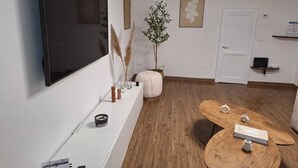 A modern living room with a flat-screen TV, a round wooden coffee table, a white bench, and a potted plant. - Cozy Corner (Nova Milanese)