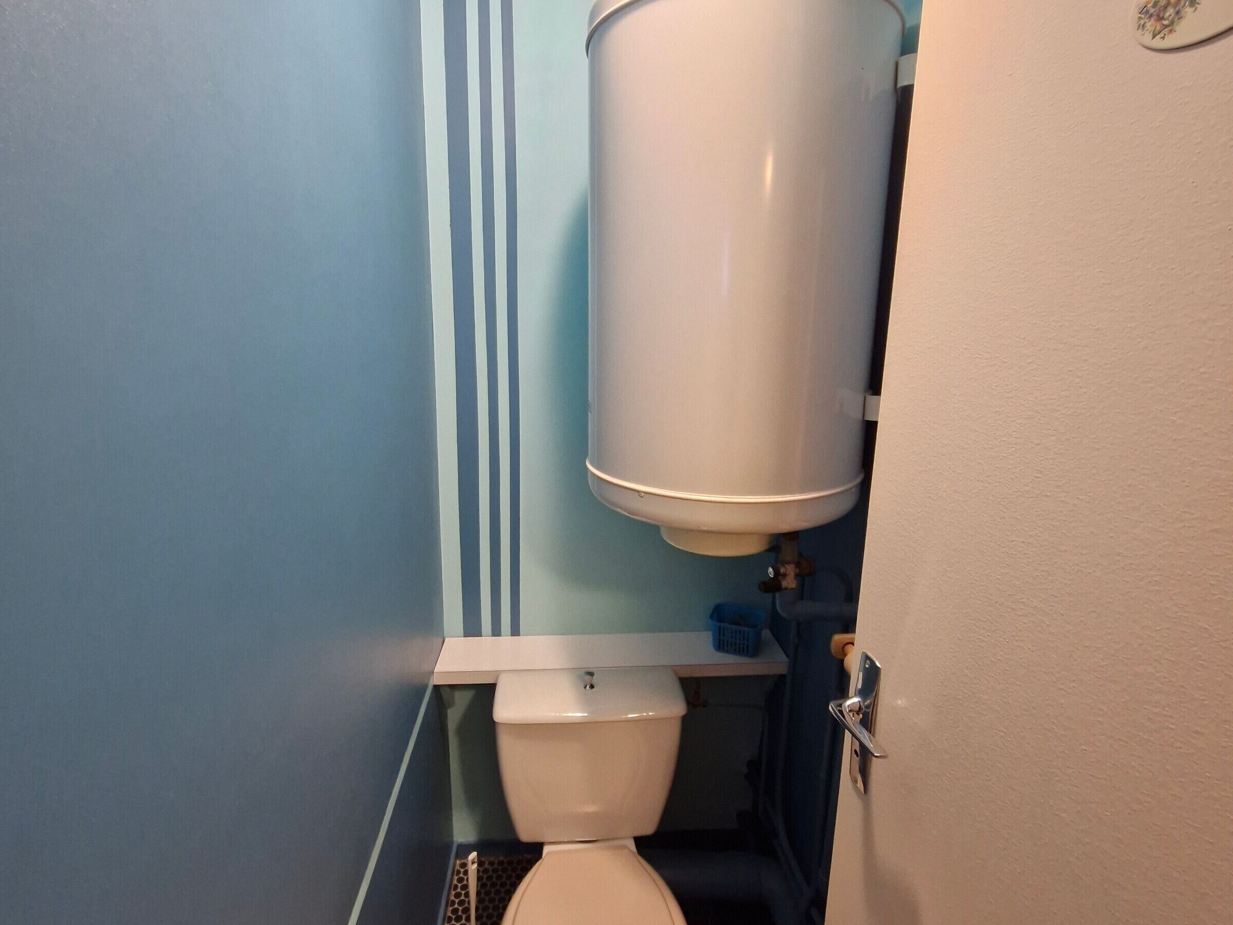 A bathroom with a toilet, a water heater, and a blue wall.