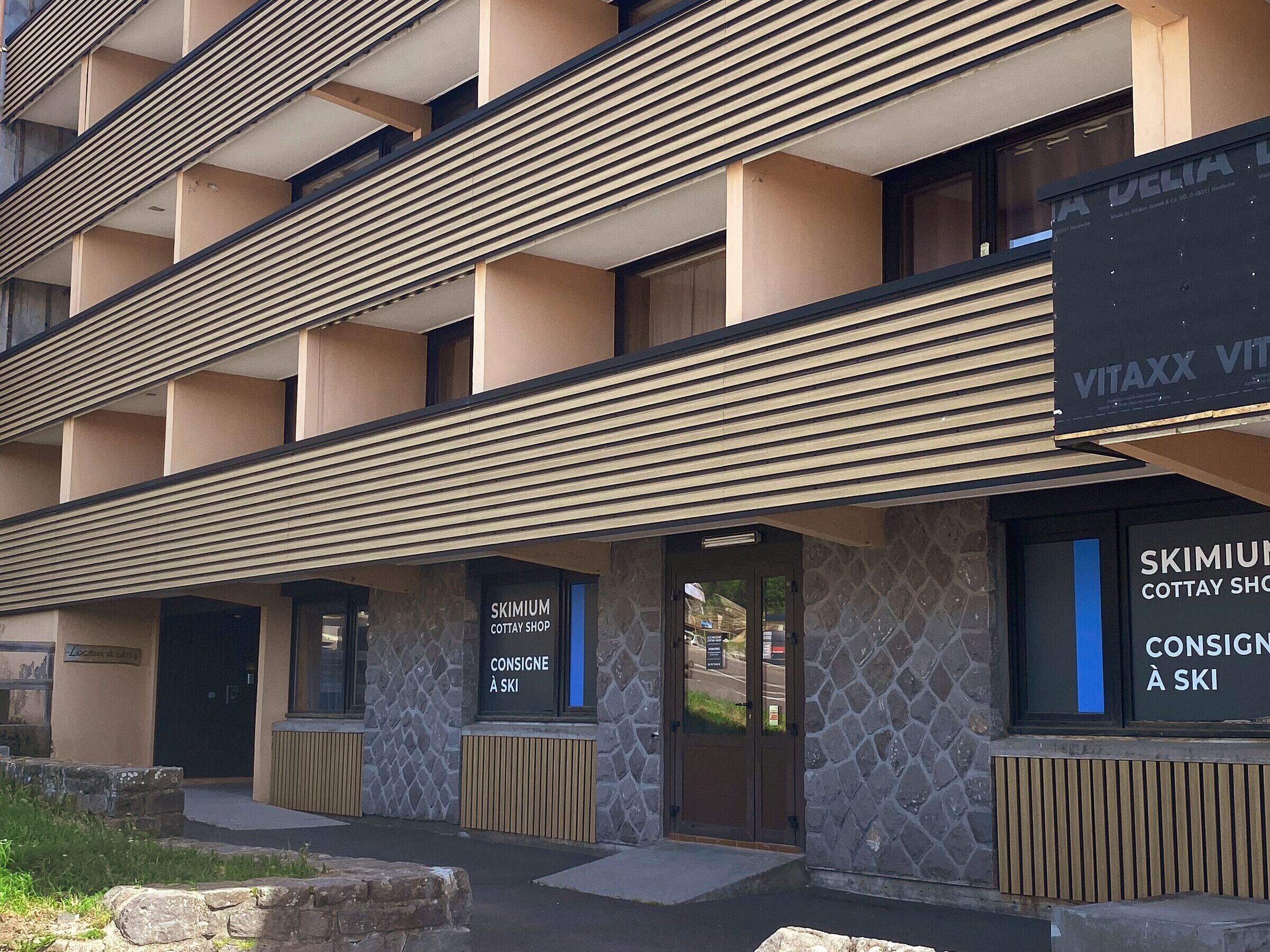 A multi-story building with a modern architectural design, featuring a stone facade and horizontal wooden slats.