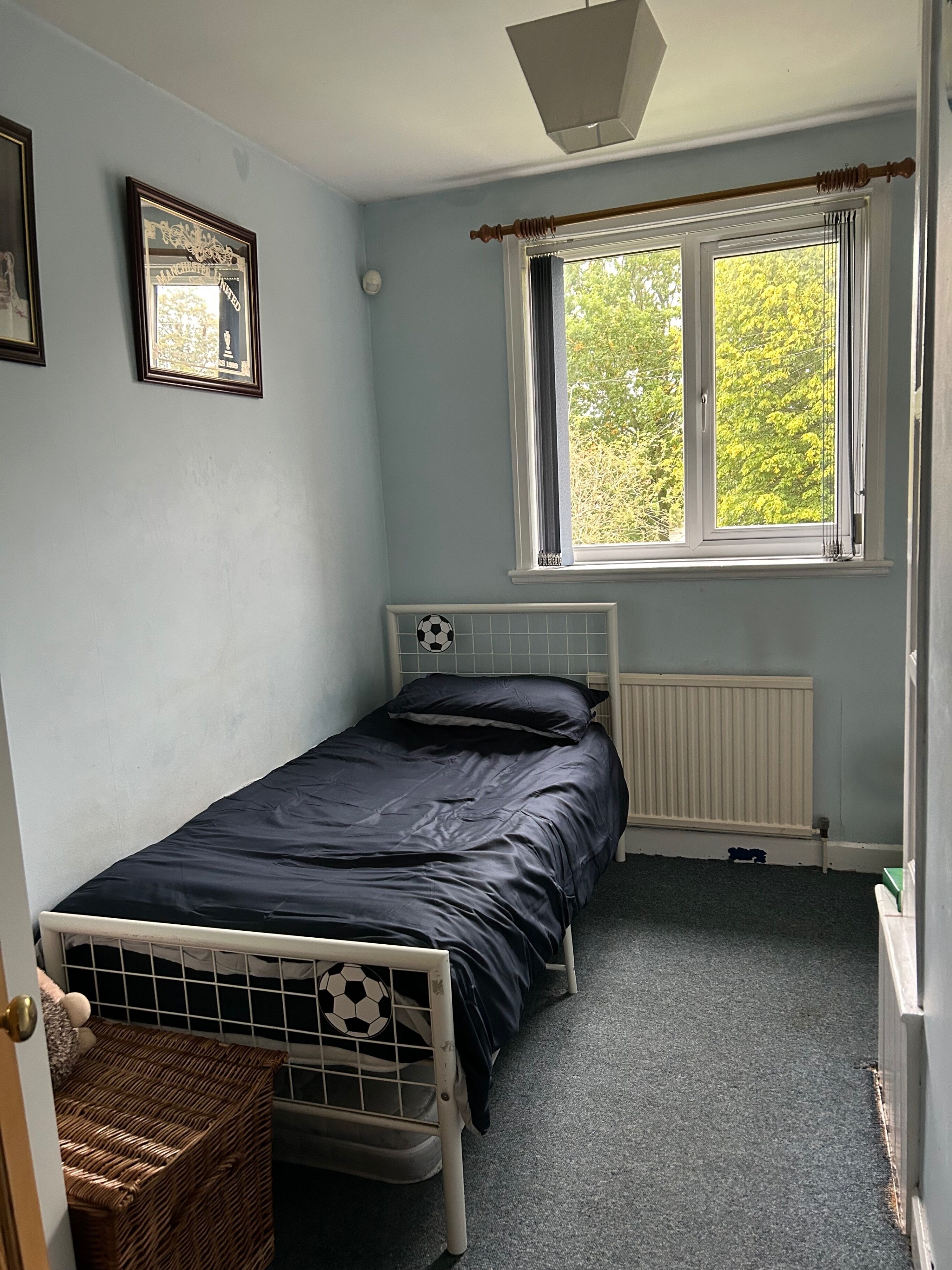 A small, single-bed room with a window, a radiator, and a soccer ball decoration.