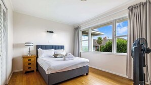 Un dormitorio con cama, mesita de noche, lámpara y ventilador de pie.
